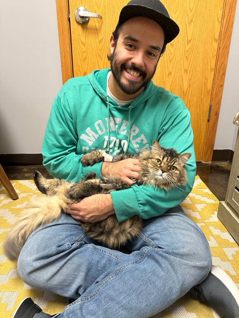 Zach, owner, cradling Max, a gray tabby, while sitting on the floor. 