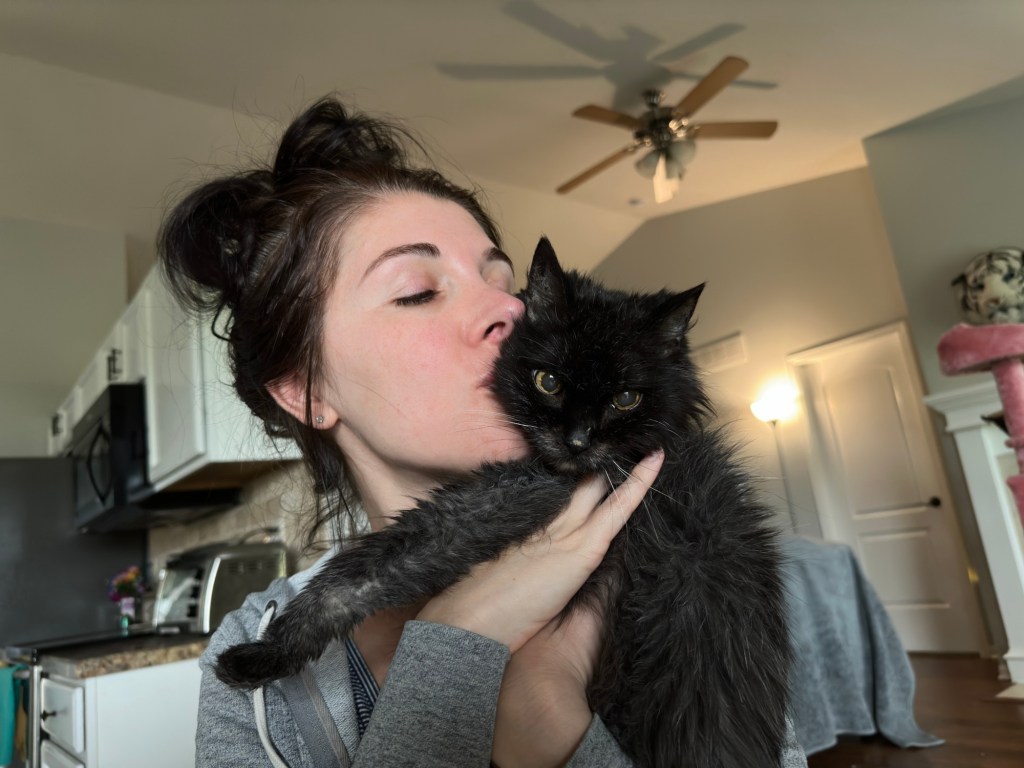 Maria, cat owner, holding and kissing Midnight, a black cat.