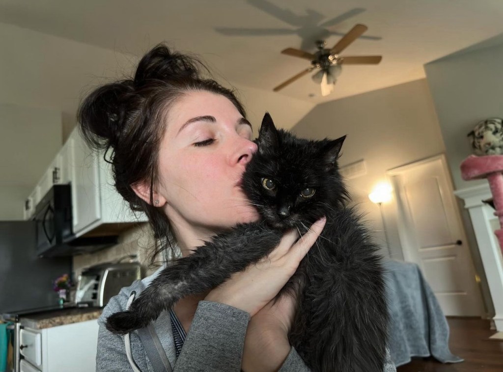Maria, cat owner, holding and kissing Midnight, a black cat.